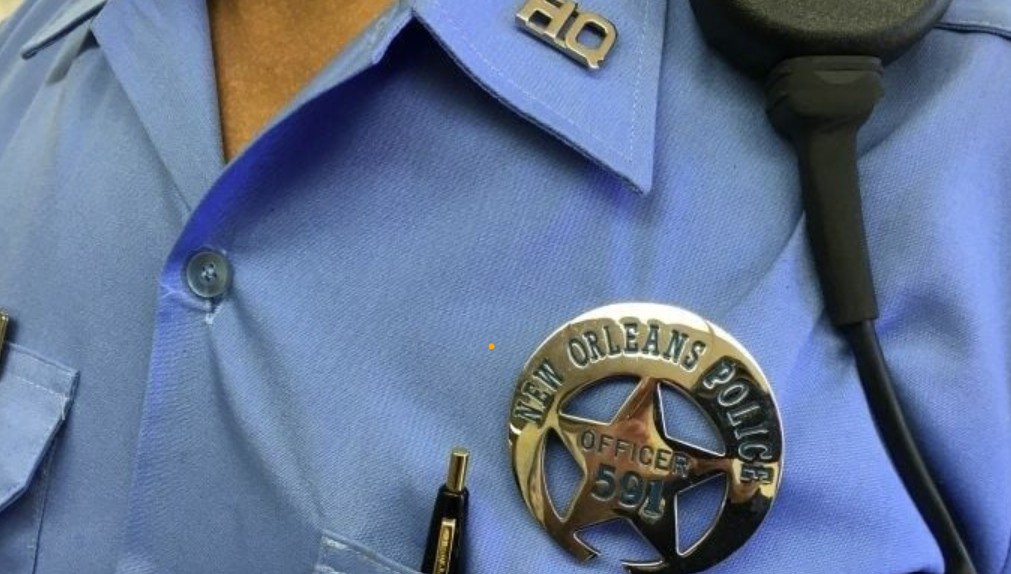 Nola.com officer file photo Photo is a close-up of a New Orleans Police Department officer, showing his light blue uniform shirt with a shiny gold New Orleans Police Department pin, which is in the shape of a crescent with a star beneath the crescent.